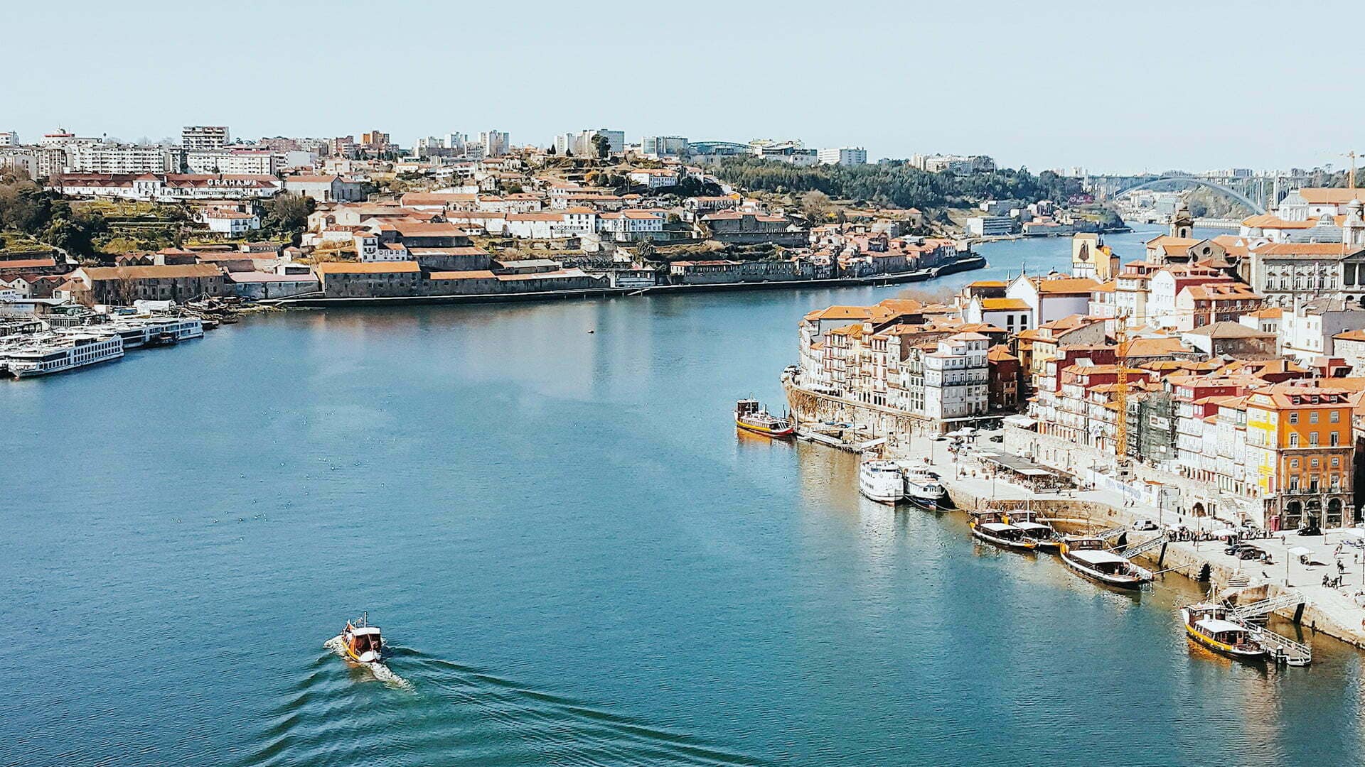 Stunning waterfront cityscape of Porto, Portugal, showcasing its vibrant real estate scene with a mix of modern high-rises and colorful historic buildings nestled along the Douro River.