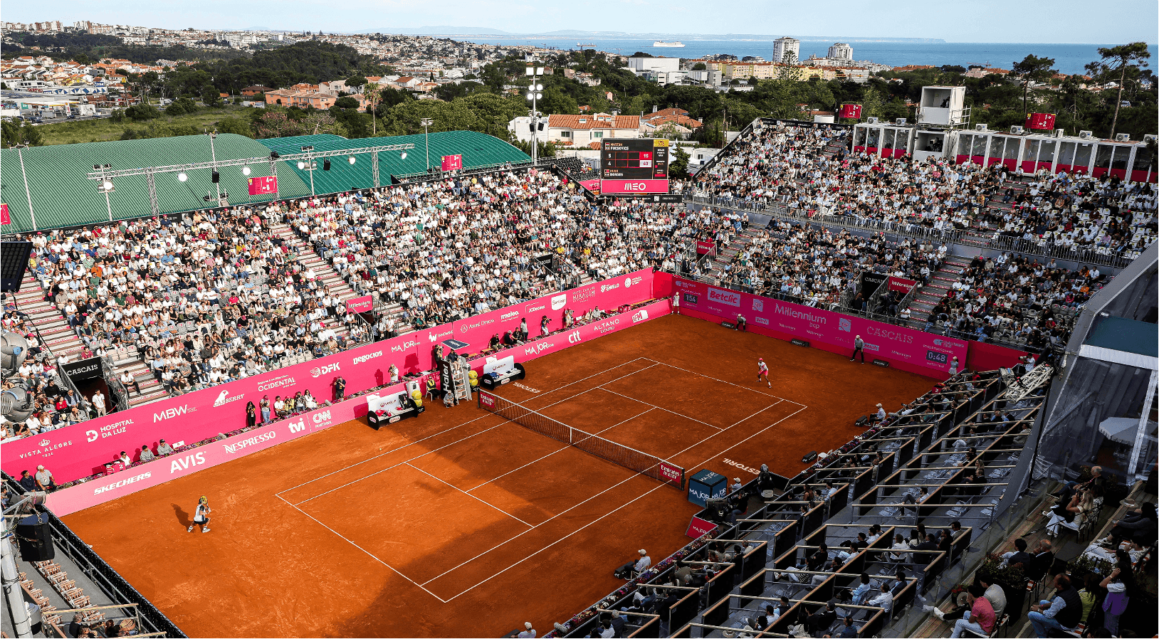 Packed clay tennis stadium overlooking coastal city
