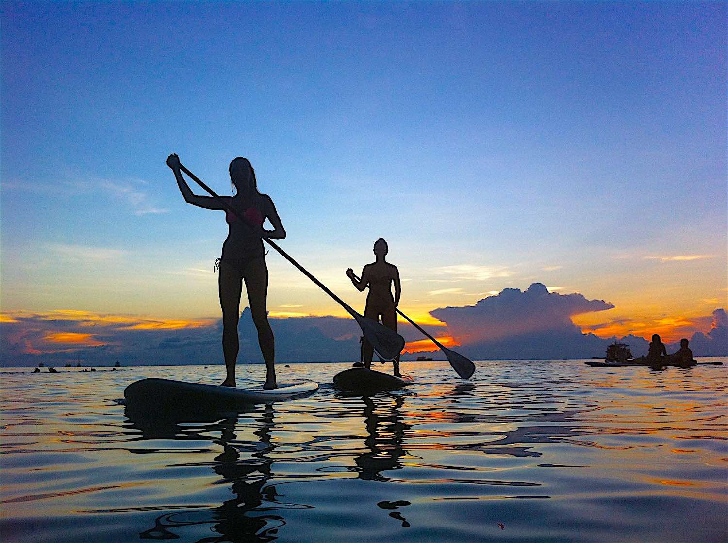 Silhouetted paddleboarders at sunset on calm sea
